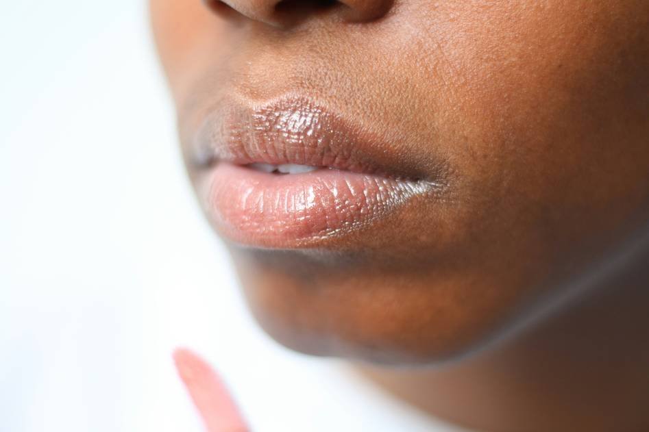 A woman applying lip plumper gloss while smiling at a vanity mirror surrounded by beauty products